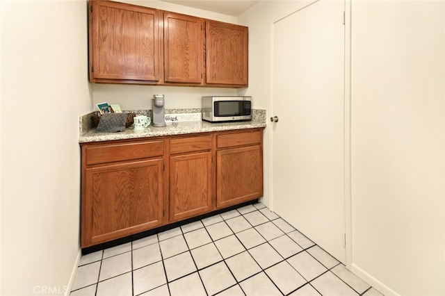 kitchen featuring light tile patterned flooring, stainless steel microwave, brown cabinets, and baseboards