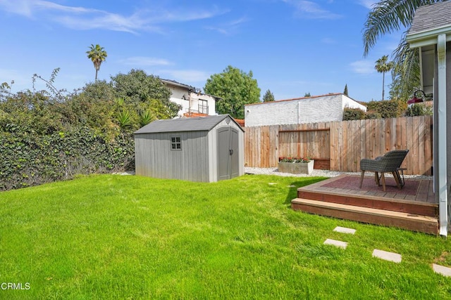 view of yard featuring a deck, a storage shed, a fenced backyard, and an outdoor structure