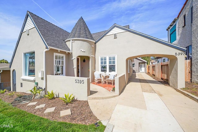 view of front facade featuring stucco siding, driveway, a shingled roof, and fence