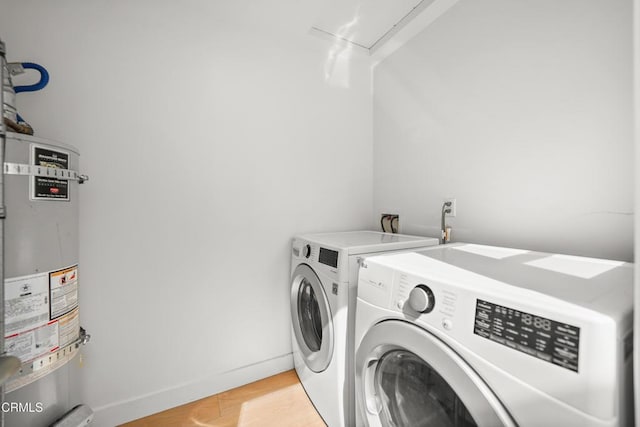 clothes washing area with strapped water heater, baseboards, laundry area, and washer and dryer