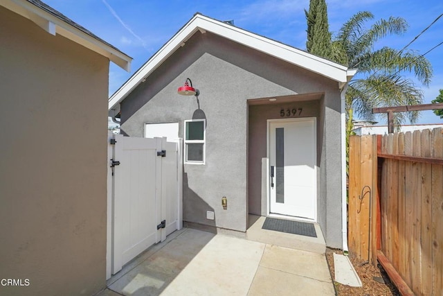 view of exterior entry with a patio area, a gate, fence, and stucco siding