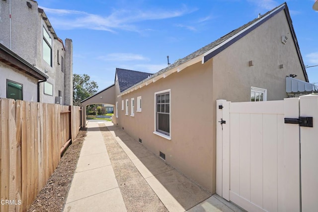 view of side of property with crawl space, stucco siding, a shingled roof, and fence