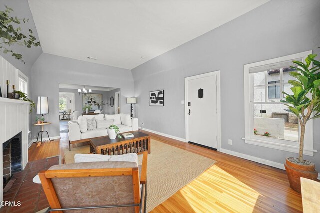 living room with a fireplace with flush hearth, a notable chandelier, wood finished floors, baseboards, and vaulted ceiling