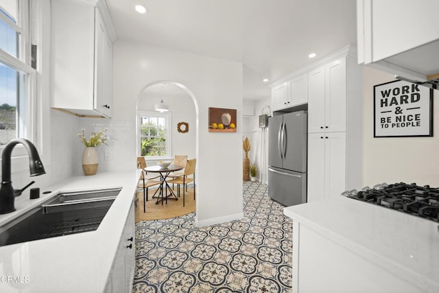 kitchen featuring a sink, white cabinetry, freestanding refrigerator, arched walkways, and light countertops