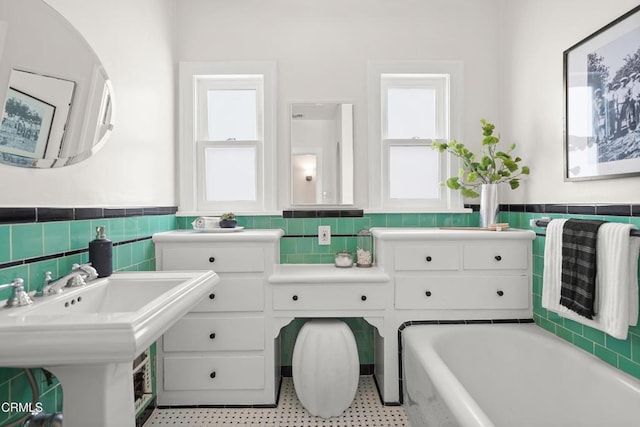 bathroom with a sink, tile walls, a bath, and wainscoting