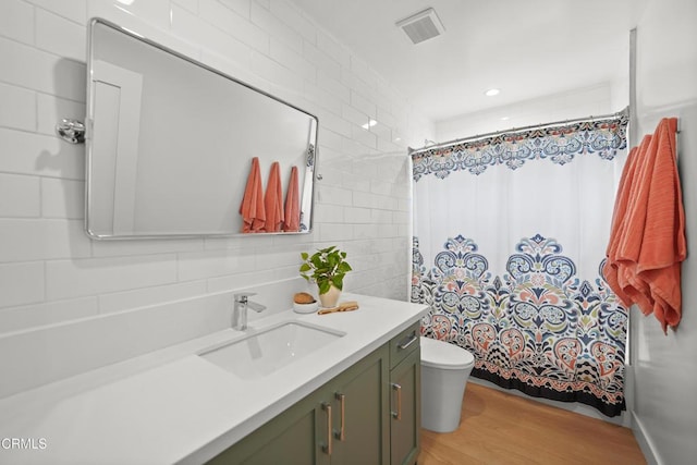 full bathroom featuring visible vents, toilet, vanity, wood finished floors, and tile walls