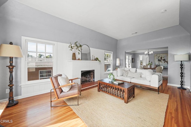 living area with visible vents, a fireplace with raised hearth, baseboards, a chandelier, and wood finished floors