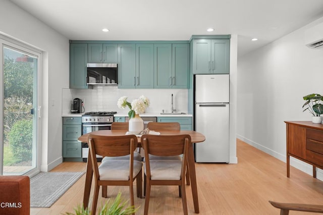 kitchen with tasteful backsplash, green cabinets, light wood-style flooring, stainless steel appliances, and a sink