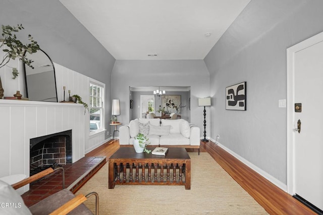 living room featuring wood finished floors, baseboards, a chandelier, and a fireplace with raised hearth