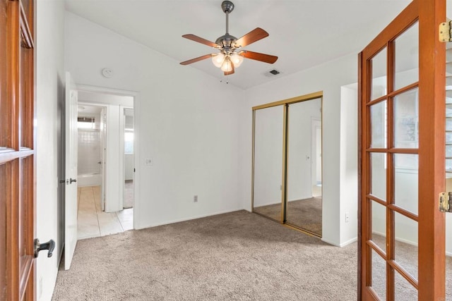 unfurnished bedroom featuring visible vents, lofted ceiling, light colored carpet, and a closet