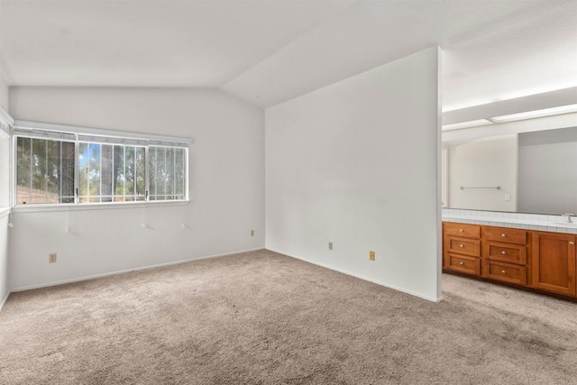 unfurnished bedroom with vaulted ceiling, light colored carpet, baseboards, and a sink