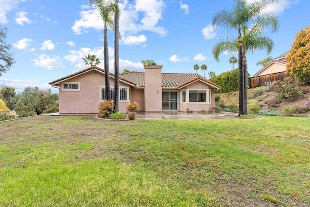 back of property with stucco siding, a lawn, a tile roof, a patio, and a chimney