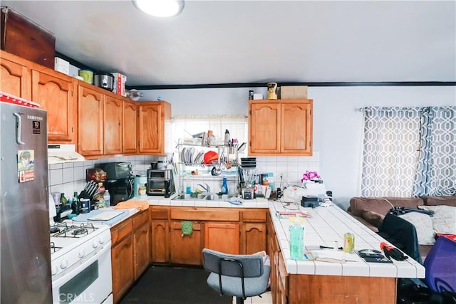 kitchen featuring gas range gas stove, tasteful backsplash, refrigerator, a peninsula, and tile counters