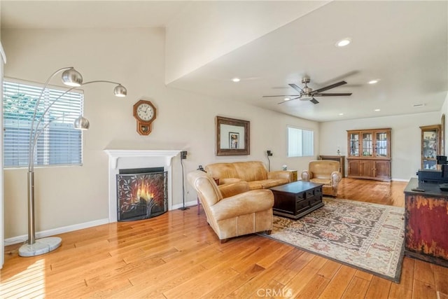 living area featuring baseboards, recessed lighting, ceiling fan, a lit fireplace, and light wood-style floors