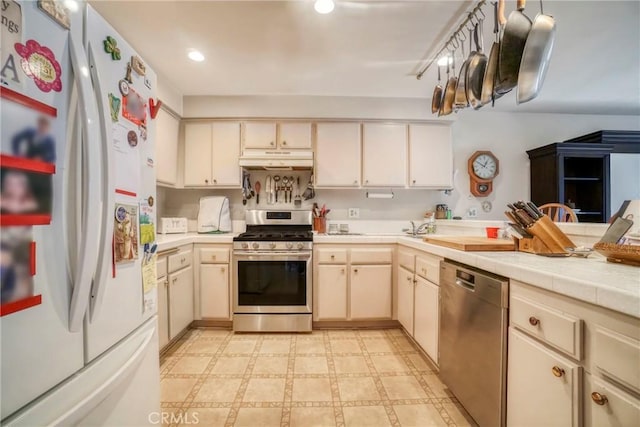 kitchen featuring light floors, a peninsula, tile counters, under cabinet range hood, and appliances with stainless steel finishes