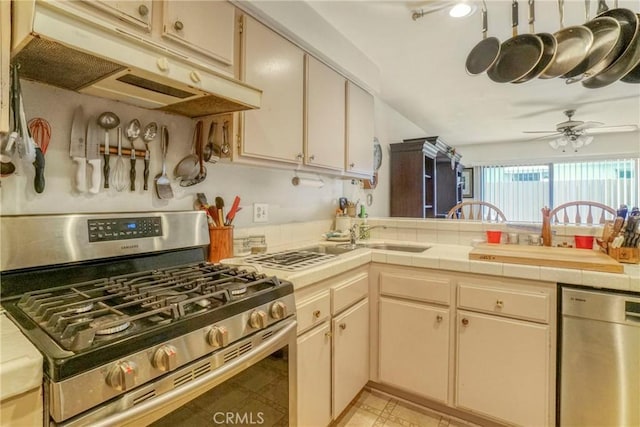 kitchen with a ceiling fan, under cabinet range hood, cream cabinets, tile countertops, and appliances with stainless steel finishes