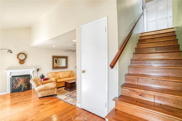 stairs with ceiling fan, a lit fireplace, and hardwood / wood-style floors