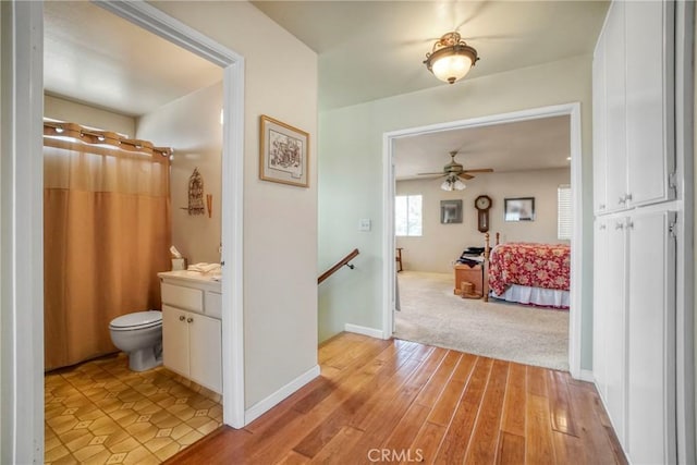 corridor with baseboards, an upstairs landing, and light wood finished floors