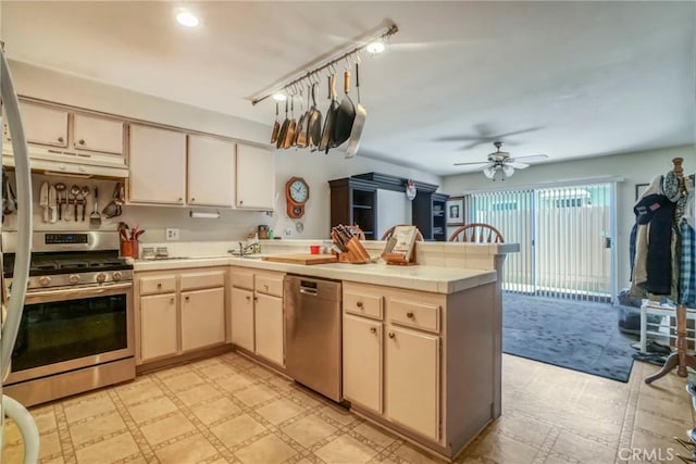 kitchen with a peninsula, light floors, appliances with stainless steel finishes, and under cabinet range hood