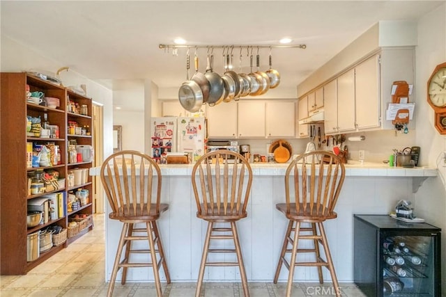 kitchen with light floors, a peninsula, freestanding refrigerator, tile counters, and under cabinet range hood