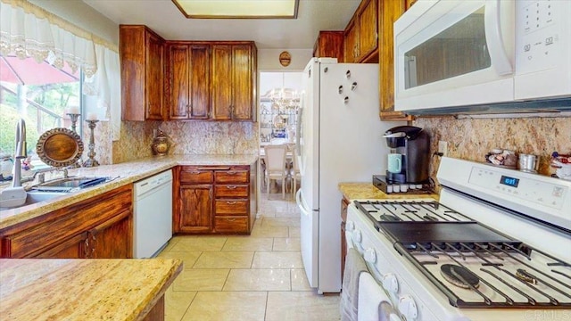 kitchen featuring white appliances, brown cabinetry, a sink, light countertops, and backsplash