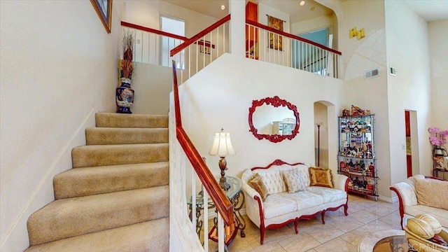 stairway with arched walkways, tile patterned flooring, a towering ceiling, and visible vents