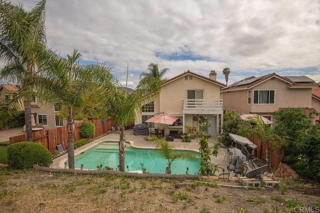 rear view of house with a fenced in pool, a fenced backyard, a balcony, stucco siding, and a patio