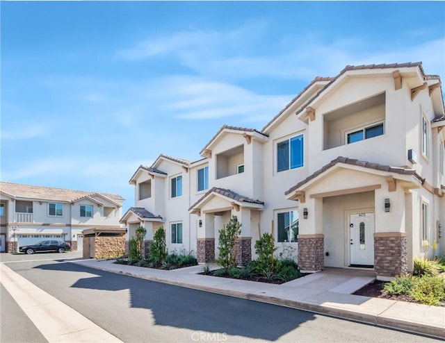 multi unit property with stucco siding, stone siding, a residential view, and a tiled roof