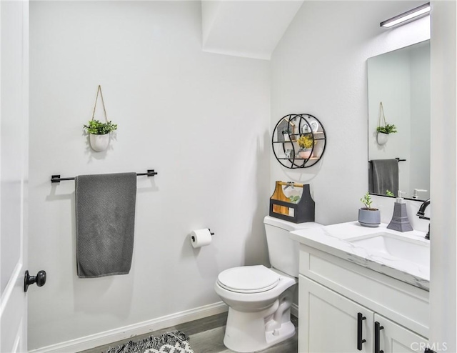 half bath with baseboards, toilet, wood finished floors, and vanity