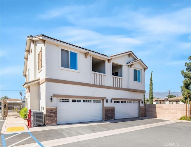 view of front of house with a gate, fence, an attached garage, stucco siding, and central air condition unit