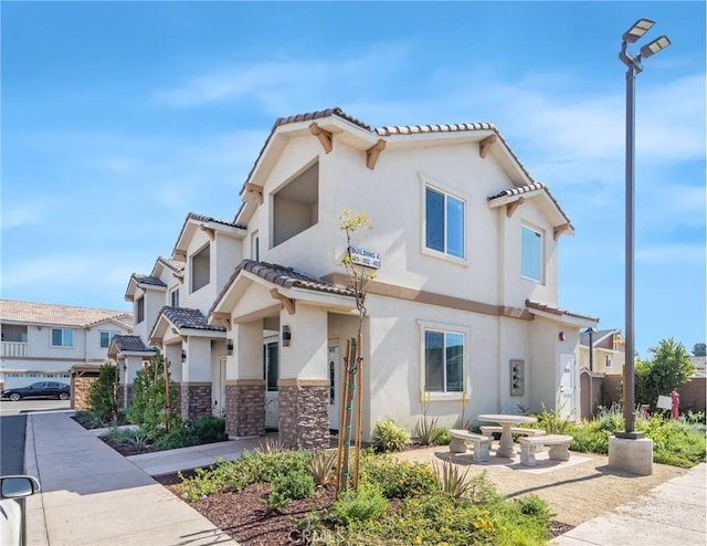 view of front of property with a tiled roof, stone siding, a residential view, and stucco siding