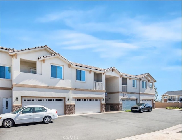 townhome / multi-family property with stone siding, stucco siding, an attached garage, and a residential view