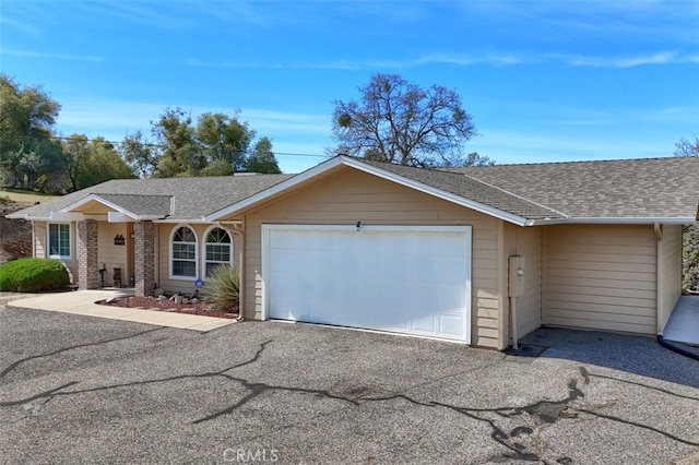 ranch-style home featuring driveway, a garage, and roof with shingles