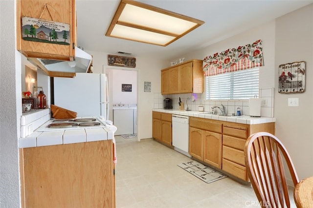 kitchen featuring white appliances, backsplash, washing machine and dryer, and tile counters