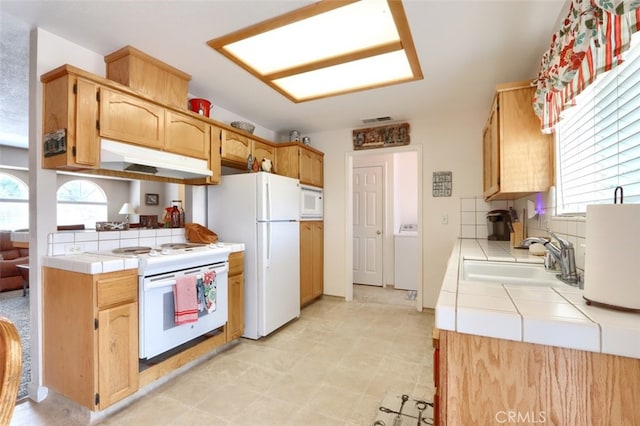 kitchen featuring a sink, white appliances, under cabinet range hood, and tile counters