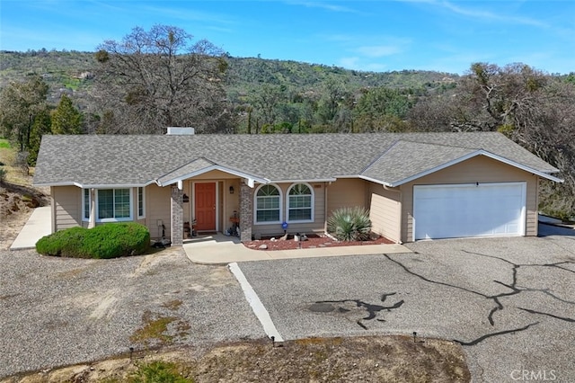 ranch-style house with driveway, an attached garage, and a shingled roof