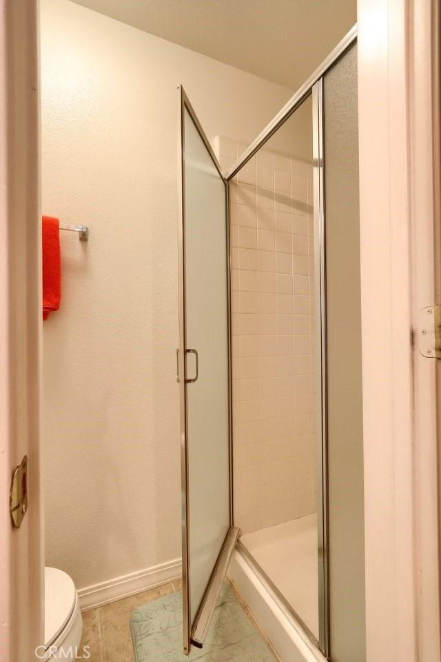 bathroom featuring tile patterned flooring, a shower stall, toilet, and baseboards