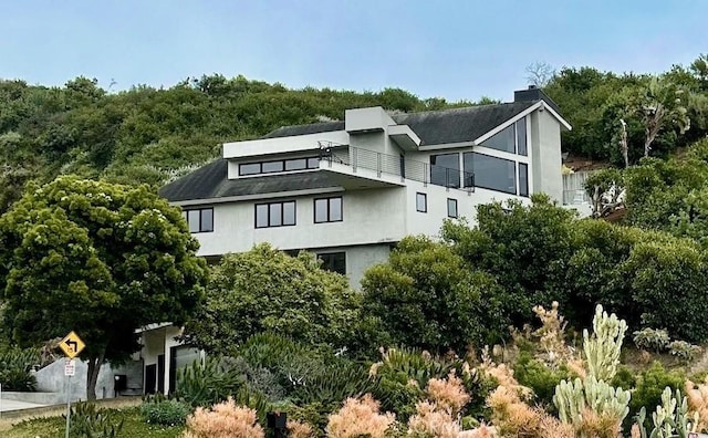 back of property with stucco siding, a balcony, and a chimney