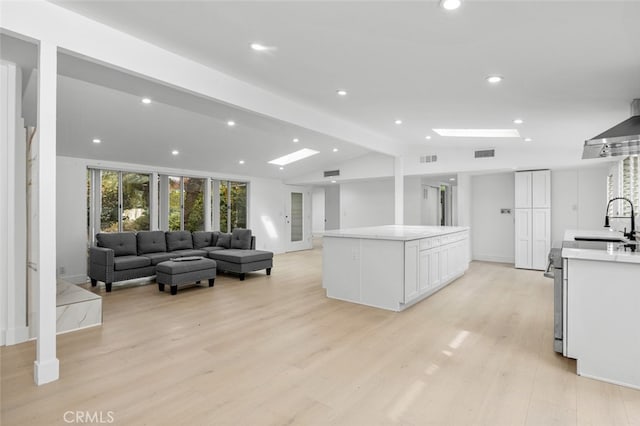 kitchen featuring light wood-type flooring, lofted ceiling with beams, a sink, white cabinets, and light countertops