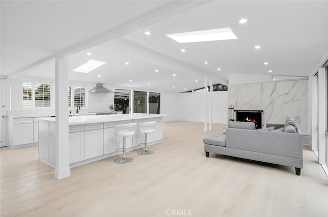 living area featuring lofted ceiling with skylight, recessed lighting, light wood finished floors, and a high end fireplace