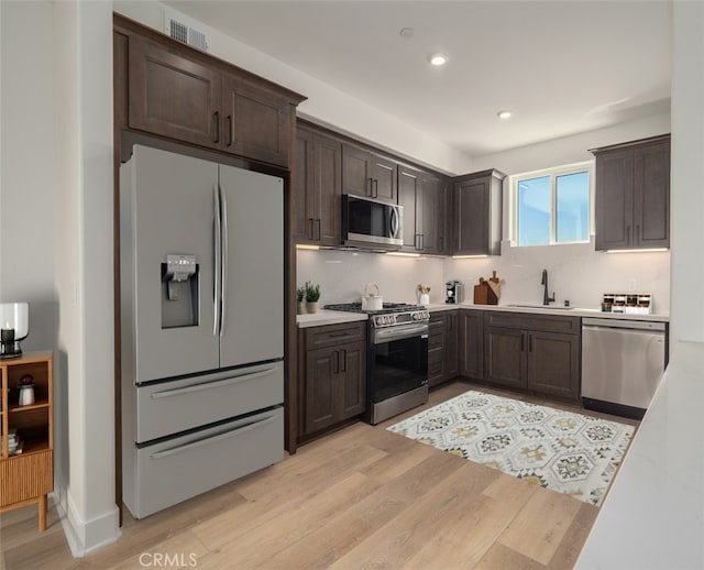 kitchen with light wood finished floors, a sink, dark brown cabinetry, light countertops, and appliances with stainless steel finishes
