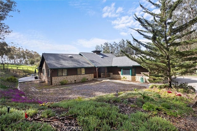 rear view of property with fence, stone siding, and roof with shingles