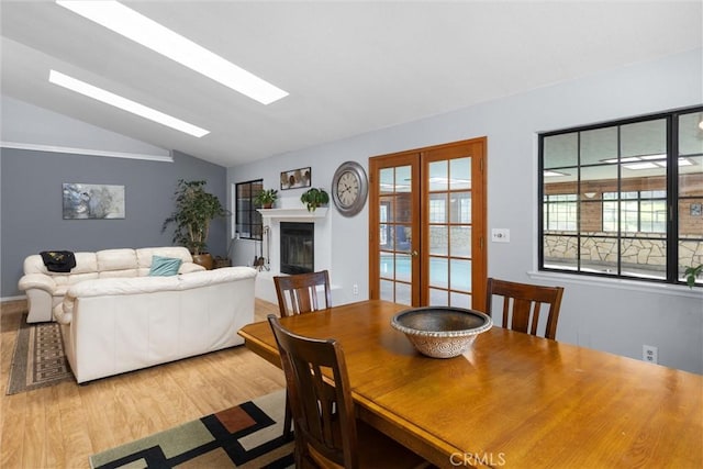 dining area with a glass covered fireplace, vaulted ceiling with skylight, wood finished floors, and french doors