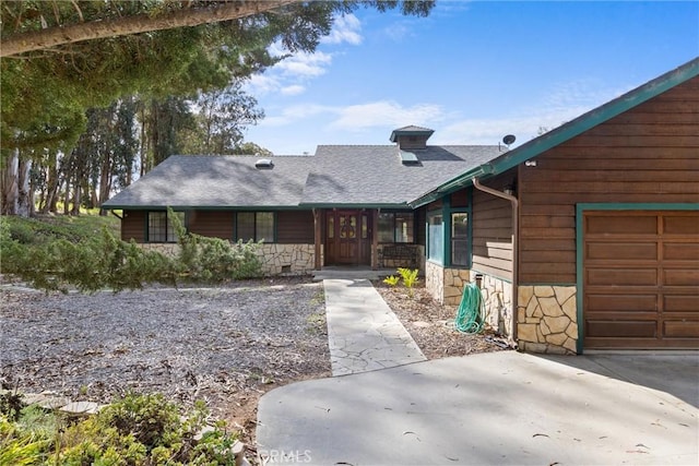 view of front of property with stone siding, an attached garage, and roof with shingles