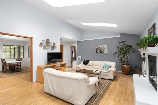 living room with a glass covered fireplace, light wood-type flooring, high vaulted ceiling, and a skylight