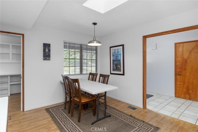 dining room featuring light wood finished floors, visible vents, a skylight, and baseboards