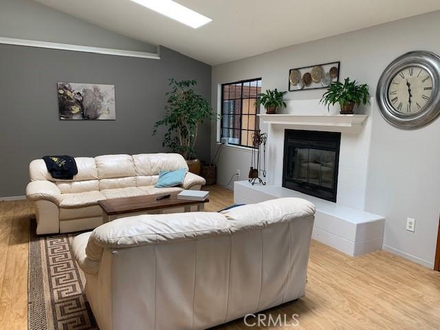 living area with a glass covered fireplace, baseboards, lofted ceiling, and wood finished floors