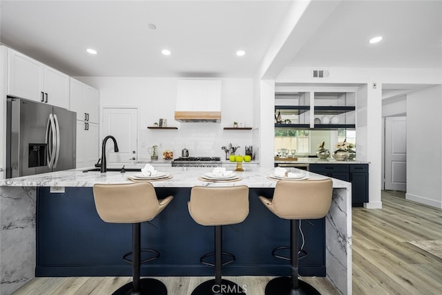 3242 Harmona Pl, Los Alamitos, CA 90720 - kitchen with stainless steel refrigerator with ice dispenser, visible vents, light stone countertops, light wood-style floors, and custom range hood