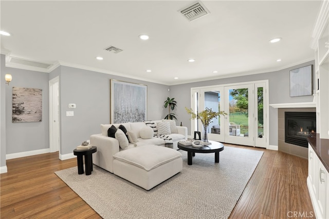 living room with baseboards, wood finished floors, visible vents, and ornamental molding