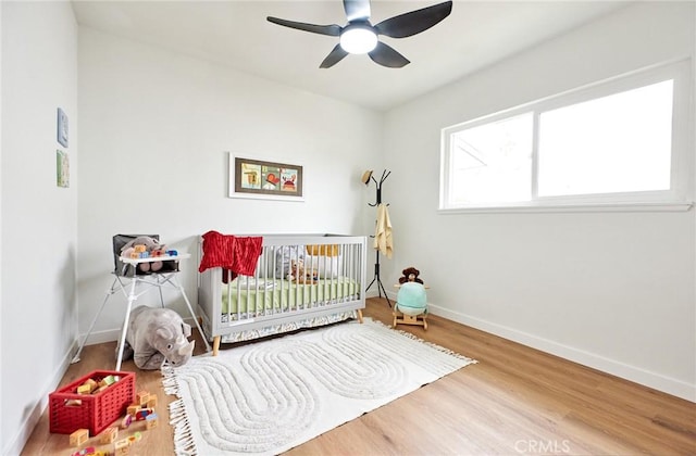 bedroom with ceiling fan, a crib, baseboards, and wood finished floors